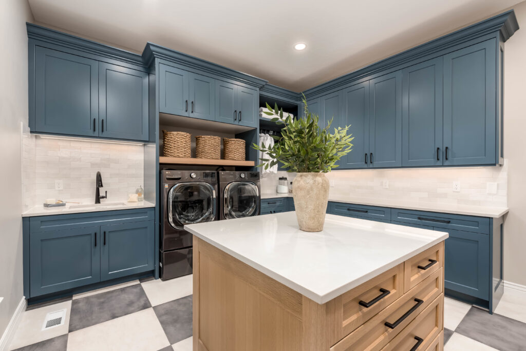 Modern laundry room featuring blue shaker cabinets, white quartz countertops, black hardware, front load washer and dryer, and built in upper storage.