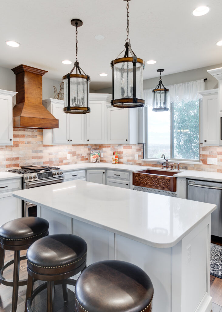 A focused shot of a white kitchen island topped with marble-look quartz, featuring three dark brown leather upholstered barstools with nailhead trim.