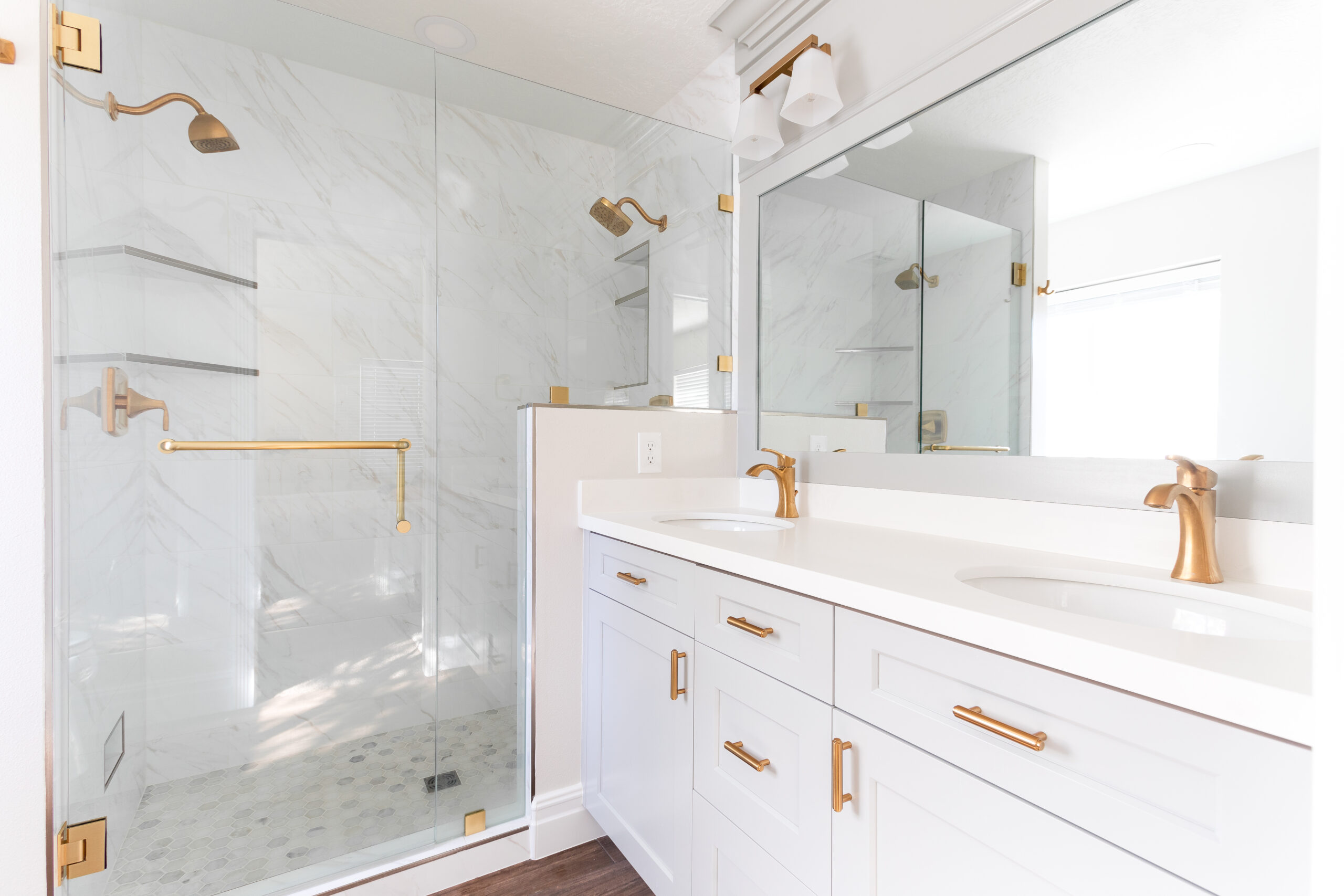 Primary bathroom remodel featuring double sink vanity, white shaker cabinetry, brushed brass hardware, and frameless glass marble shower.