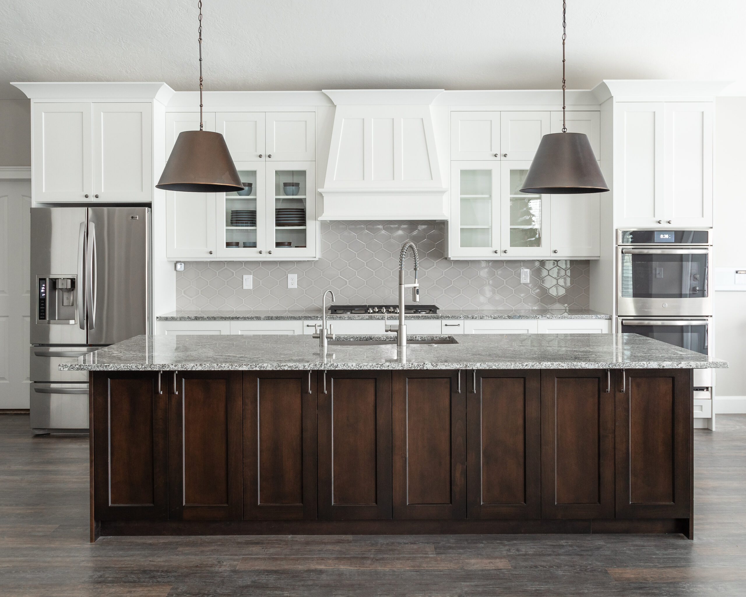 Bright kitchen with white shaker cabinets, custom range hood surround, granite countertops, and hexagon tile backsplash.